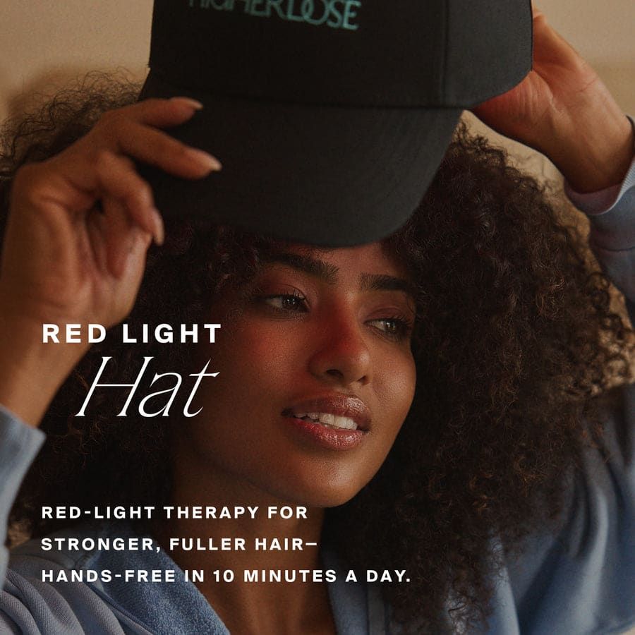 A woman wearing the HigherDOSE Red Light Hat at home, with red light visible under the peak.